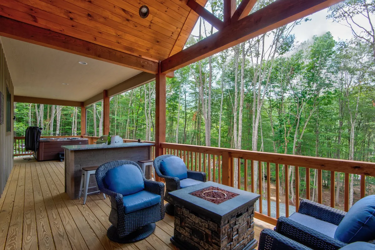 A spacious wooden deck with a cozy seating area surrounds a glowing fire pit, all framed by tall trees. The setting is perfect for social gatherings, relaxation, and outdoor activities, with enough space for family and friends to enjoy nature together.