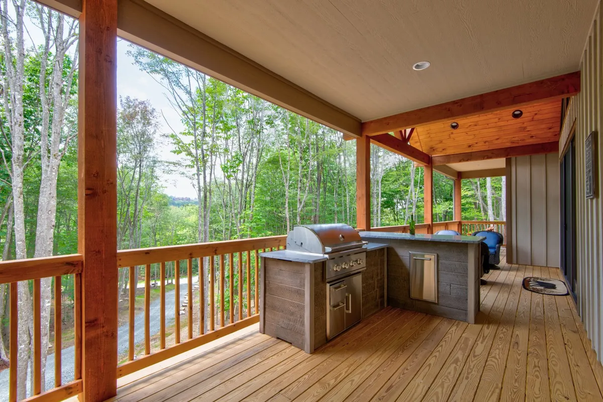 An outdoor grill area and wooden deck with comfortable seating, wooden railings, and a serene wooded backdrop—perfect for al fresco dining, grilling, and socializing while enjoying the fresh mountain air.