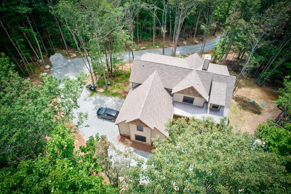 This exterior image displays the welcoming house structure nestled among mature trees, with a sunlit gravel driveway leading up to the peaceful porch. The setting is ideal for families arriving, mingling outdoors, or returning from resort-style adventures nearby.