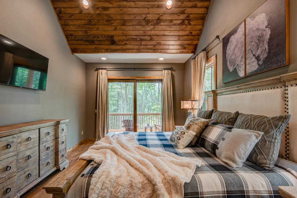 An inviting bedroom with plush bedding, a large window with a scenic view, a wooden dresser, and decorative wall art. The room is designed for comfort and tranquility, with space to relax or enjoy quiet moments.