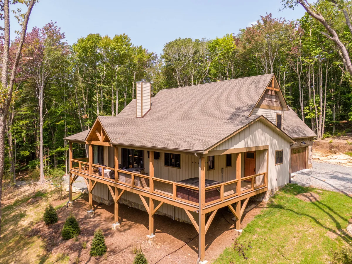 The image captures a wooden porch surrounded by lush natural scenery and a classic stone chimney, inviting relaxation and outdoor enjoyment. The porch overlooks the expansive grounds, creating a tranquil atmosphere ideal for spending time with pets.