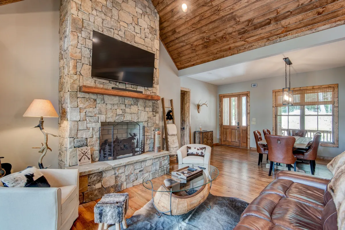 A warm dining area set beside a striking stone fireplace and framed by wooden beams. The rustic table is ready for group meals, surrounded by an inviting atmosphere that encourages festive gatherings and memorable feasts.
